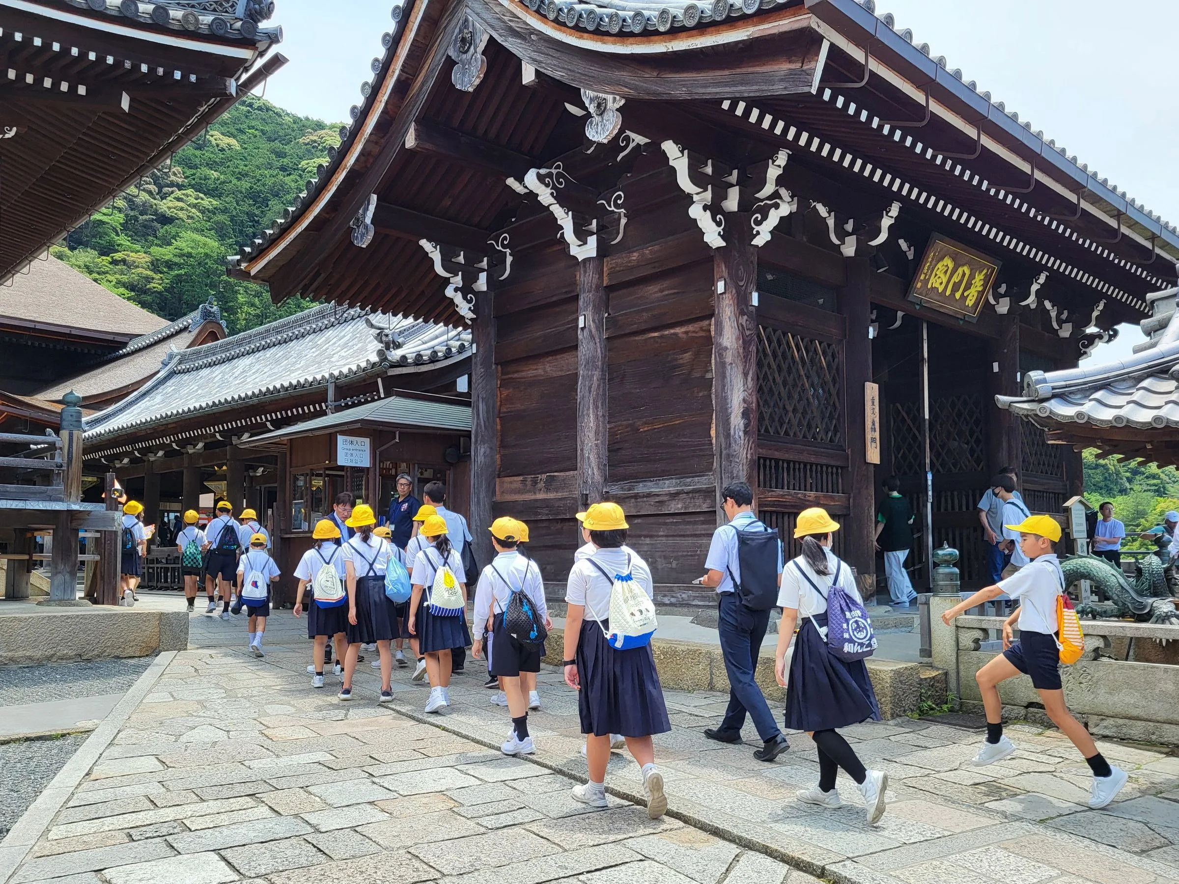 A class of schoolchildren in yellow caps walking together into Kiyomizu-dera, Kyoto