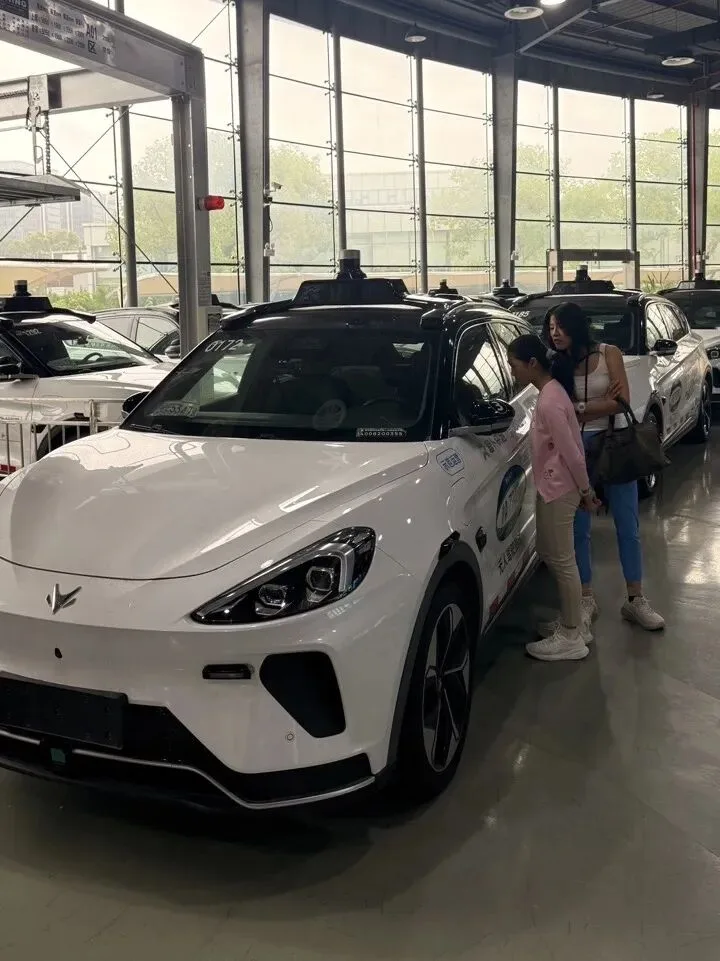 A fleet of white robotaxis with roof-mounted lidar parked in a glass-walled hangar