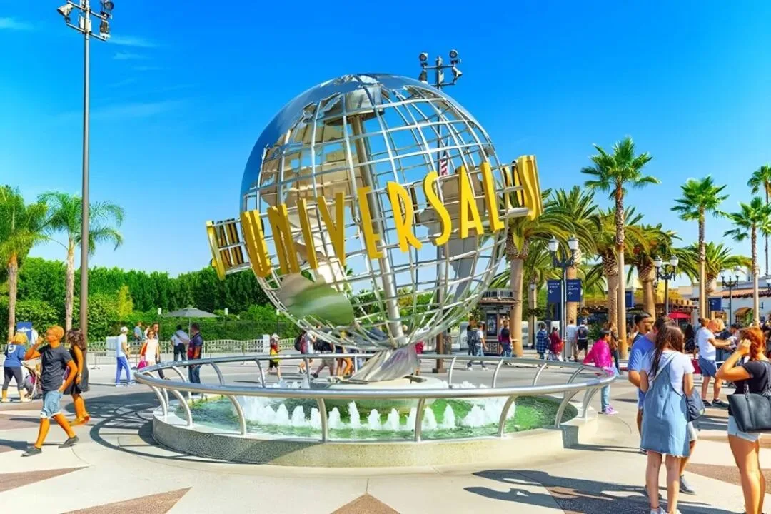 Visitors passing the revolving Universal globe and its fountain under palm trees.