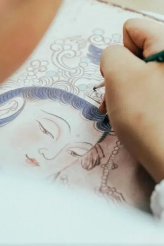 Brush layering blue-grey colour into the hair of a drawn deity's face