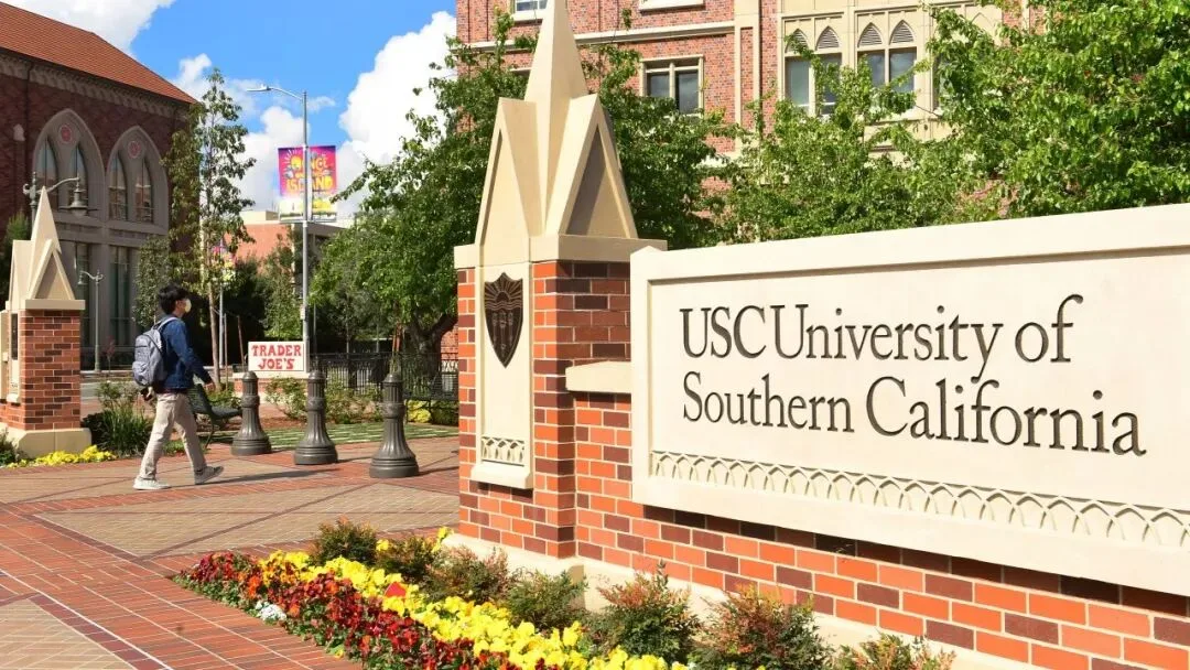 The USC University of Southern California entrance sign beside brick buildings and flowerbeds.