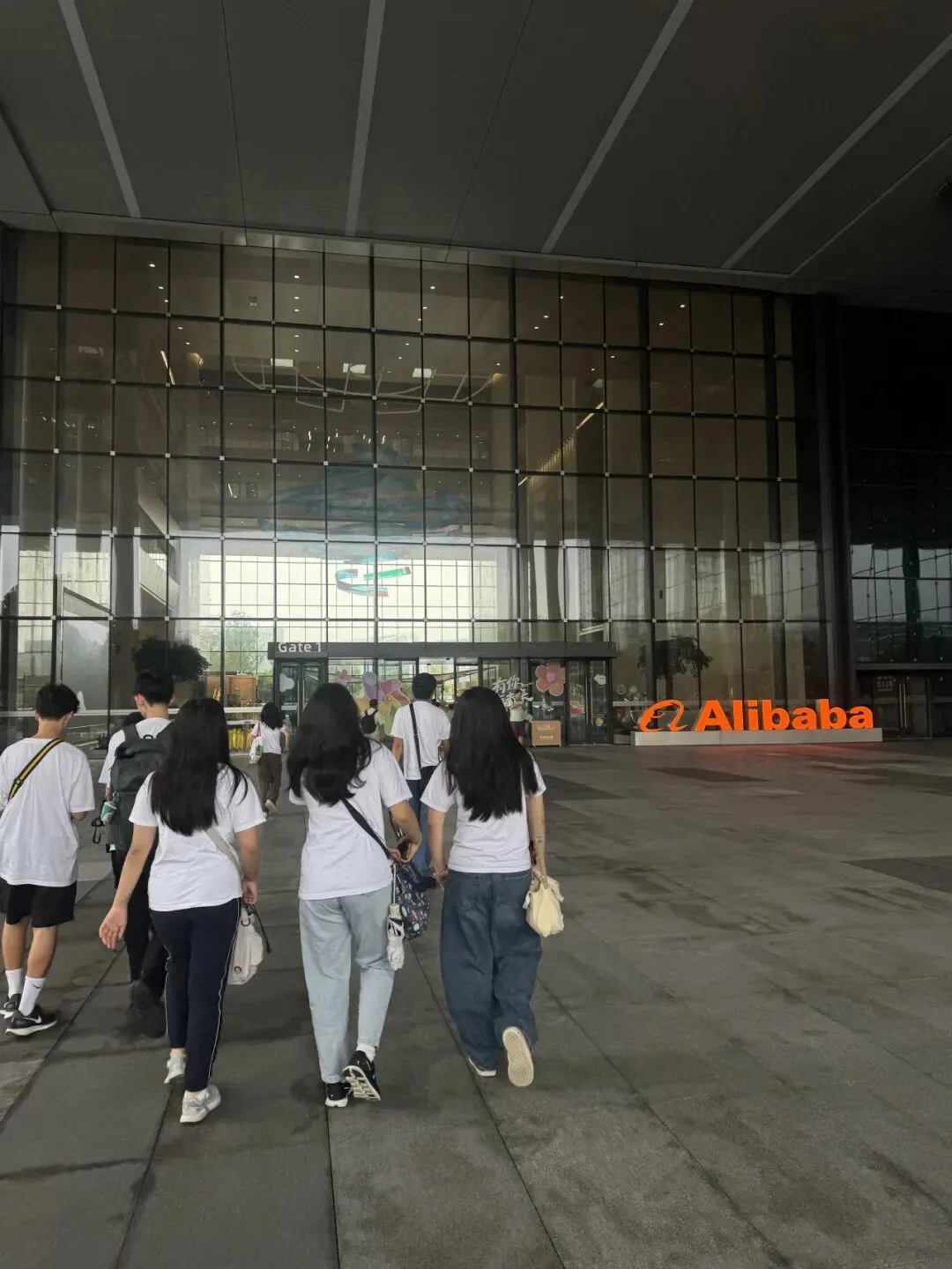 Students in matching white shirts walk toward the glass entrance of the Alibaba campus