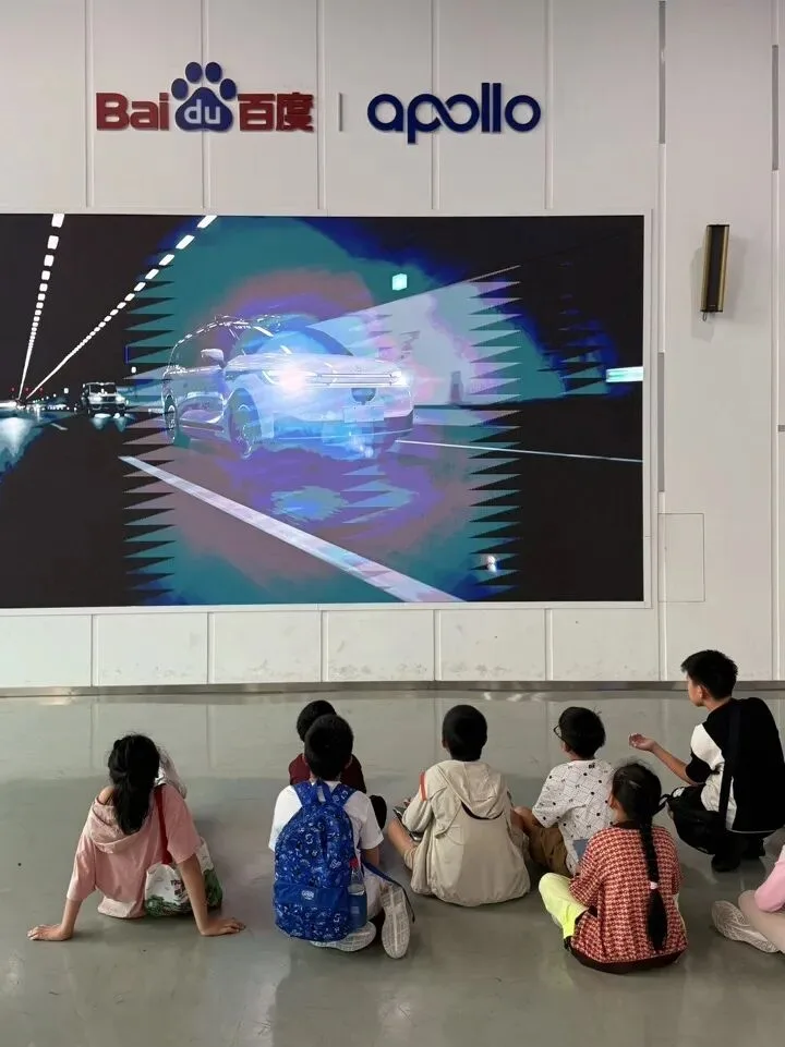 Children sit on the floor watching a screen showing a car mapped by lidar at Baidu Apollo