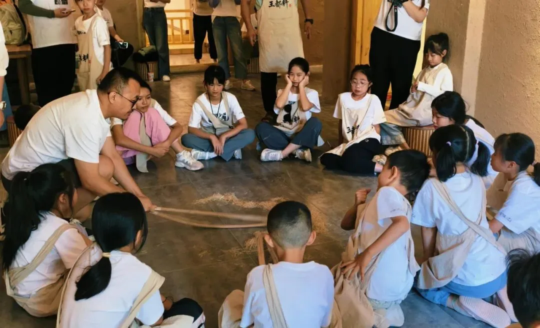 Instructor and children sitting in a circle on the floor around a bundle of straw fibre