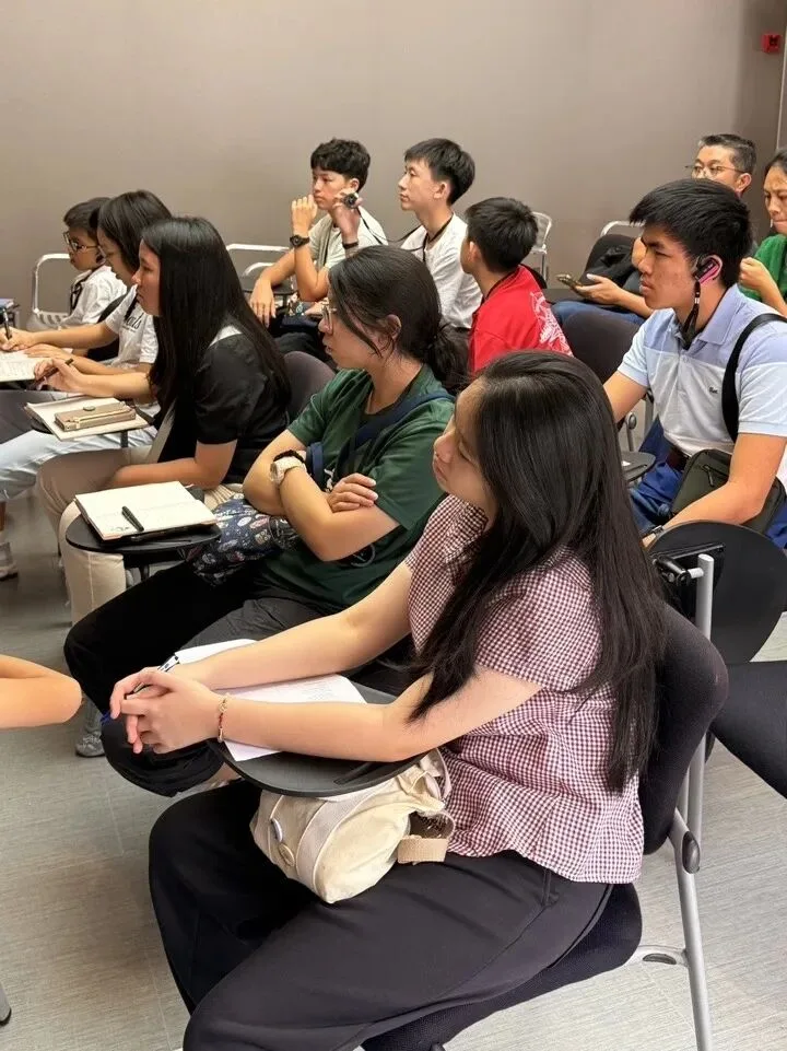 Students sit with notepads listening to a talk in a plain lecture room