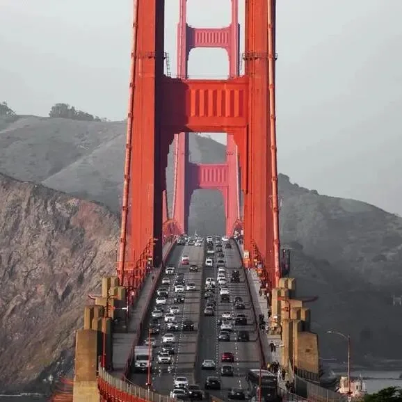 Traffic crossing the Golden Gate Bridge beneath its red tower, headlands rising behind.