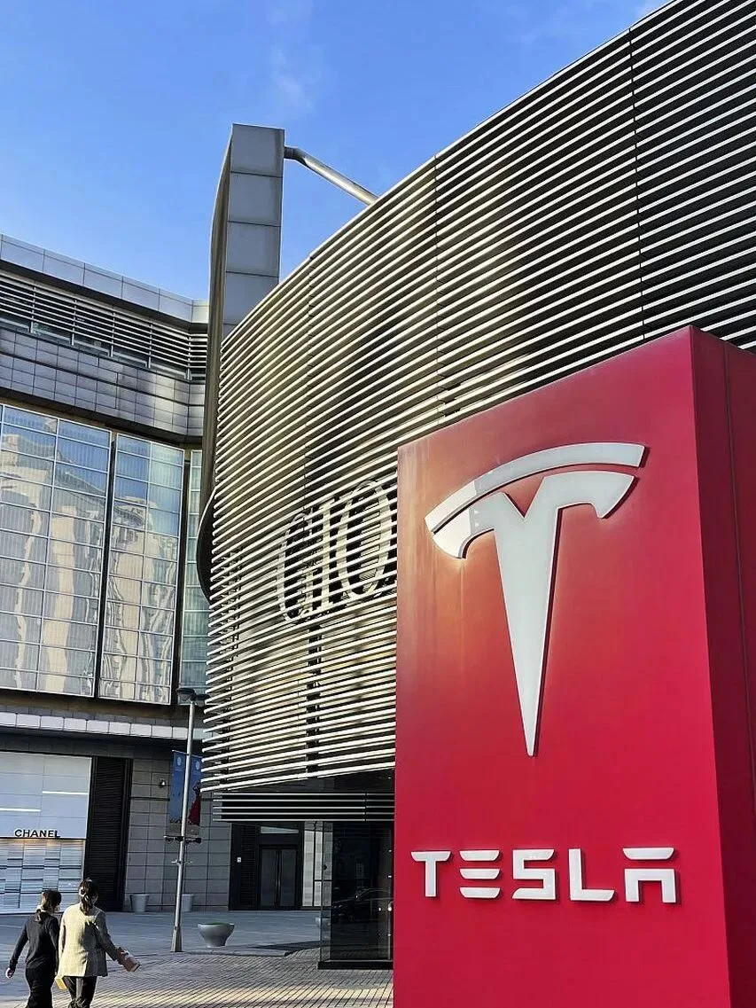 A red Tesla sign outside a louvred building, with a Chanel storefront further along the street.