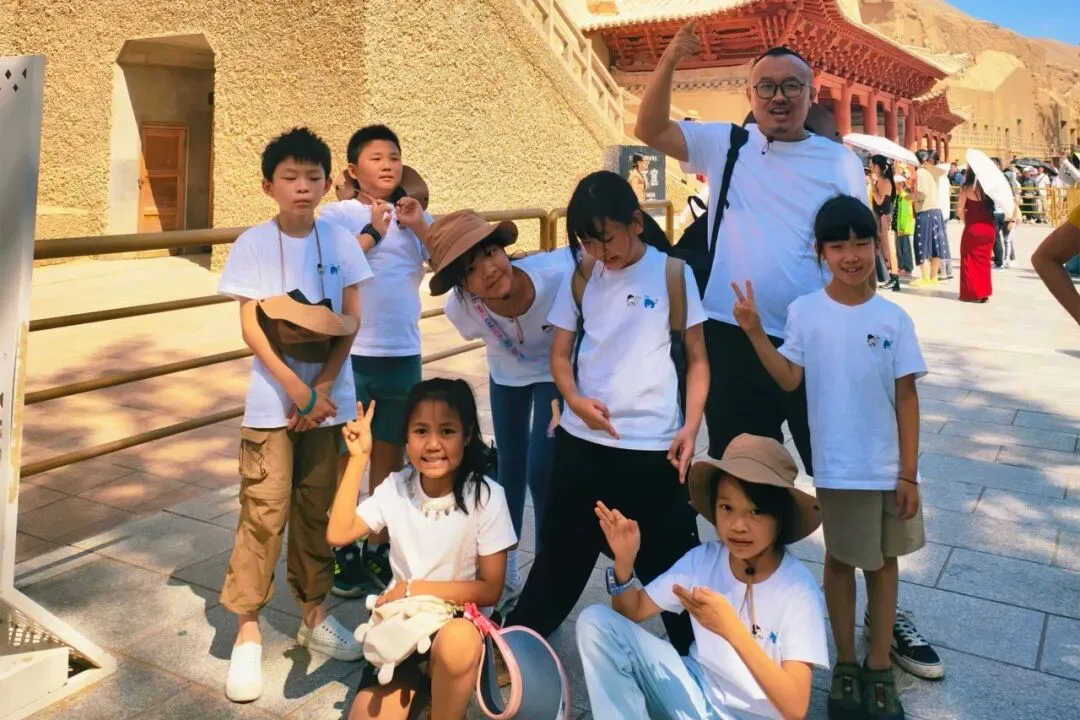 Children and their guide posing in front of the tiered temple facade at the Mogao Caves