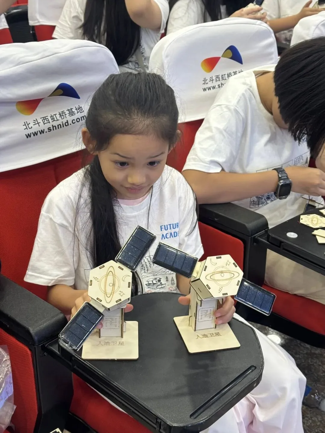A girl holds two wooden satellite models she assembled at the BeiDou West Hongqiao Base