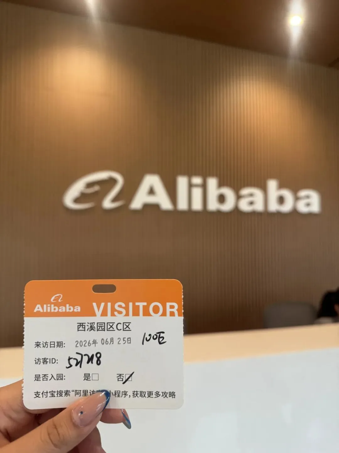 A hand holds an Alibaba visitor pass for Xixi Campus Zone C dated 25 June 2026