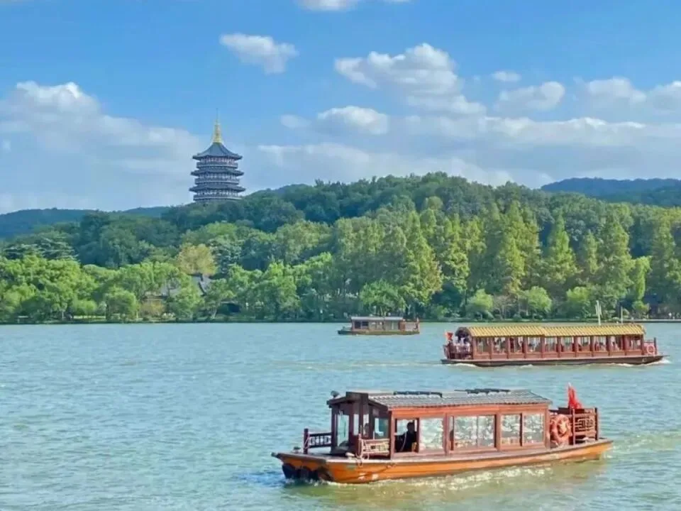 Wooden tour boats cross West Lake below Leifeng Pagoda on its wooded hill