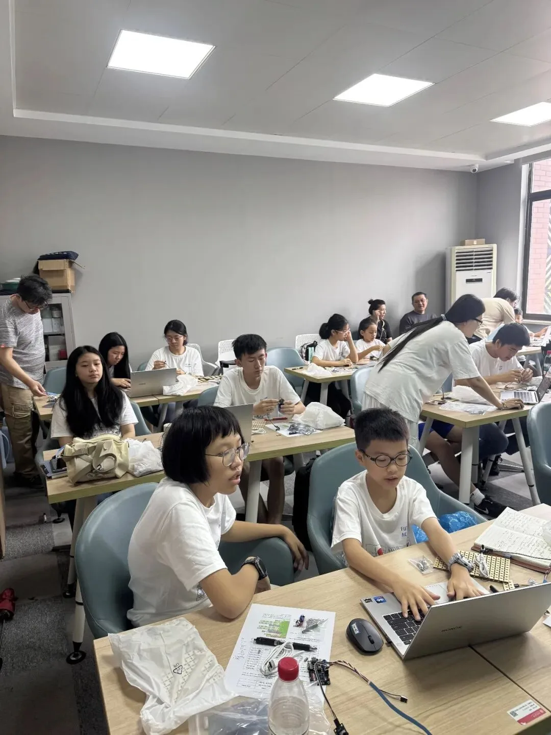 Students work with laptops and electronics kits at desks in a university classroom