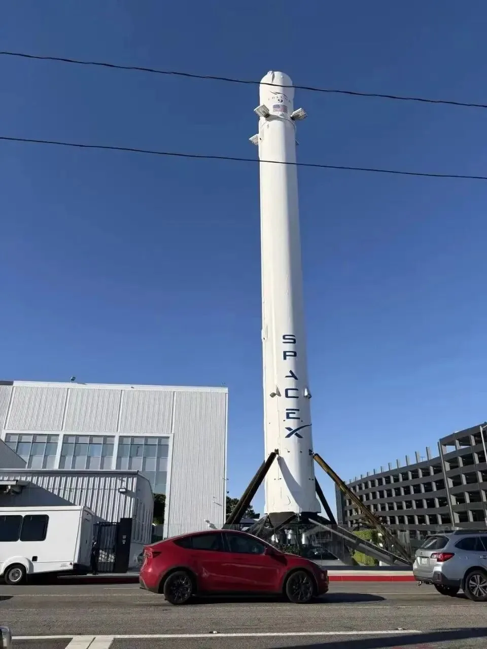 A Falcon 9 booster standing on its landing legs outside the SpaceX headquarters building.
