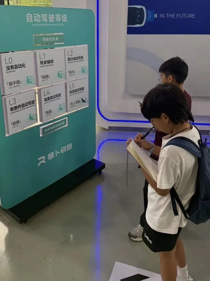 A student takes notes beside a board explaining autonomous driving levels L0 to L5