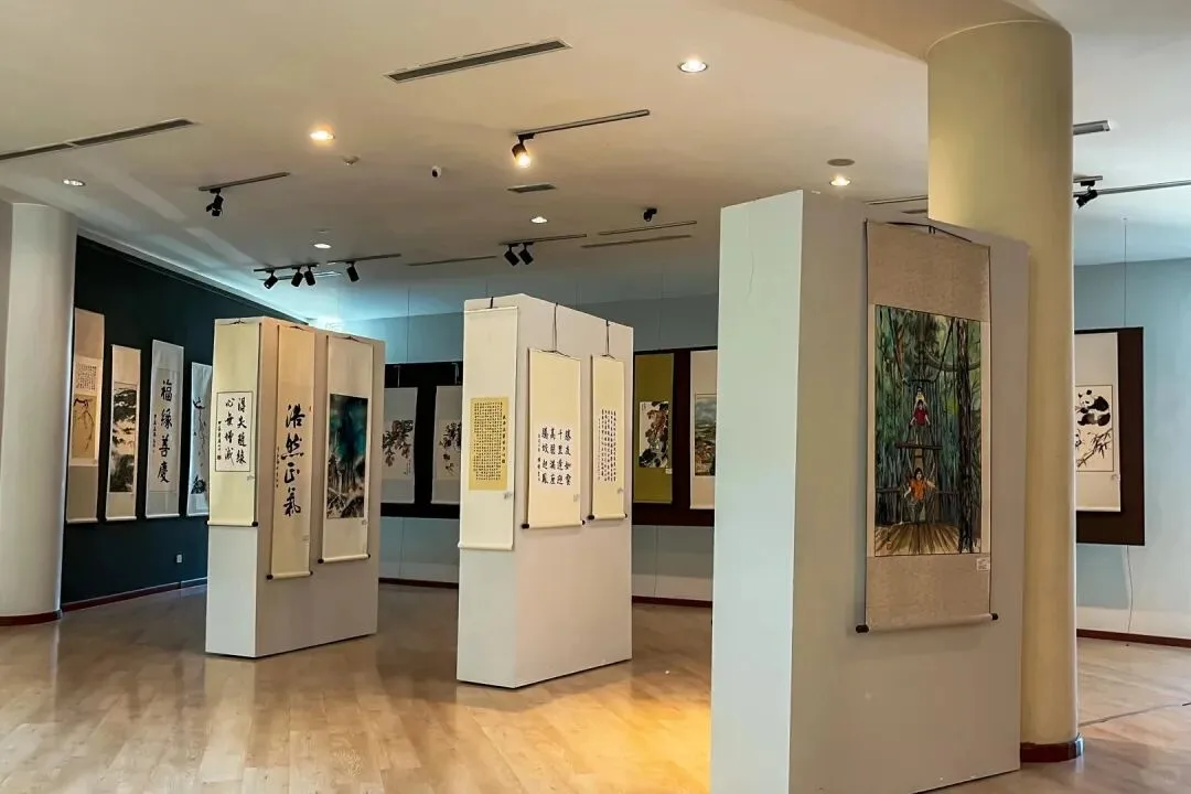 Gallery interior with Chinese calligraphy and ink-painting scrolls hung on free-standing partitions and walls.