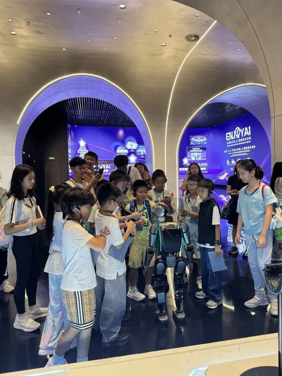 Children crowd around a small humanoid robot in the EnjoyAI showroom's arched, purple-lit hall