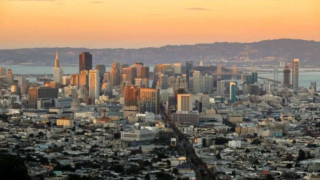 San Francisco's downtown and the Bay Bridge at sunset, seen from the hills above the city.