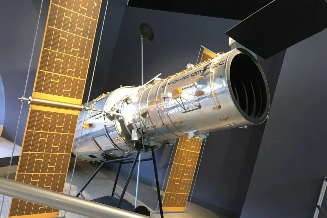 A full-size space telescope model with gold solar arrays on museum display.