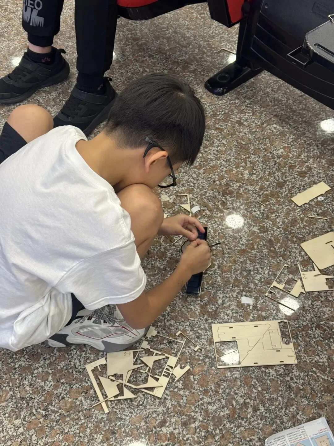 A boy kneels on the floor fitting together laser-cut plywood satellite parts