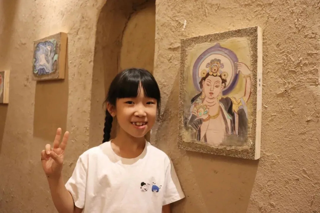 Girl beside her finished bodhisattva panel hung on an earthen cave wall