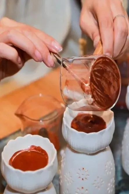 Red-brown pigment poured from a glass beaker into small fluted white bowls