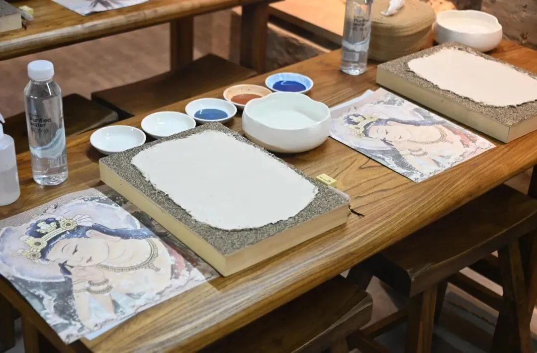 Two primed clay boards on a table with dishes of blue and red pigment and printed reference sheets