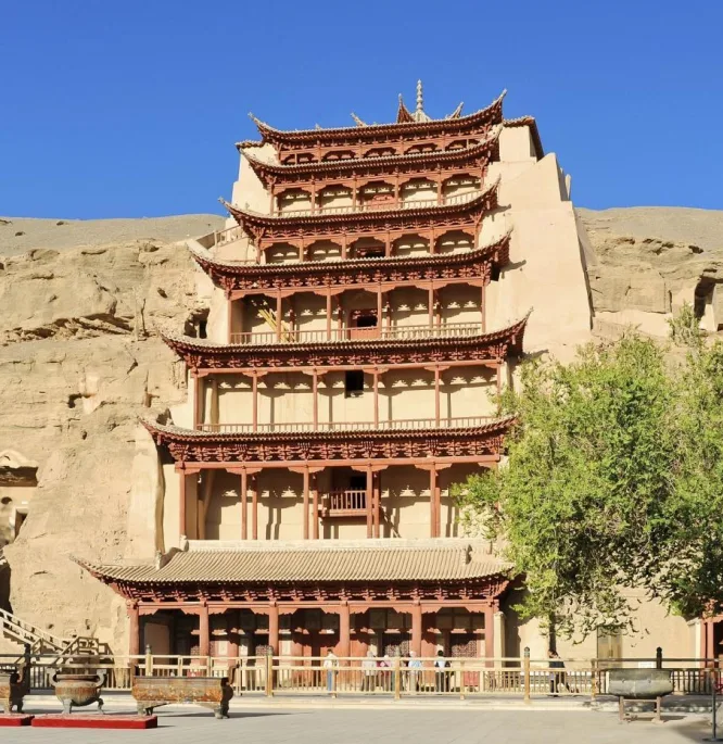Nine tiers of red timber balconies built into a desert cliff face, visitors gathered below
