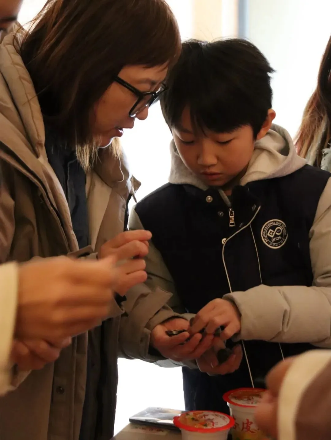 A woman and a boy inspecting small bronze tokens in their palms at the bazaar counter