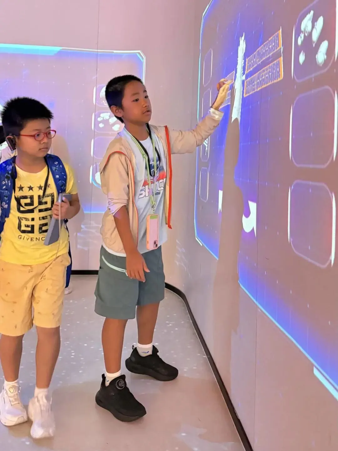 Two boys at an interactive touch wall, one reaching up to tap the glowing screen