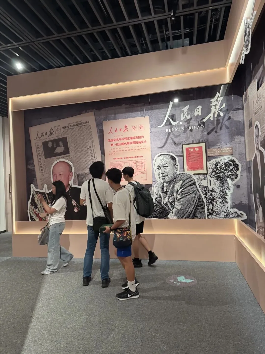 Visitors stand before a museum wall of People's Daily front pages and cut-out portraits