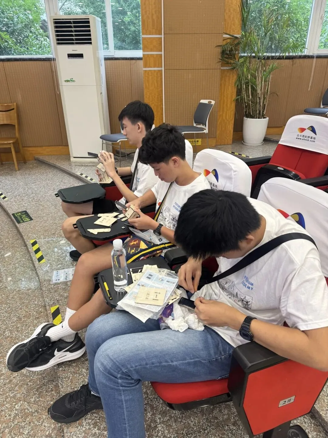 Three teenagers work through their satellite model kits from lecture-hall seats