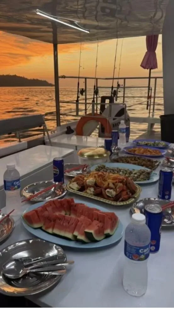 Dinner laid out on a boat deck at sunset: watermelon, seafood platters and cold drinks.