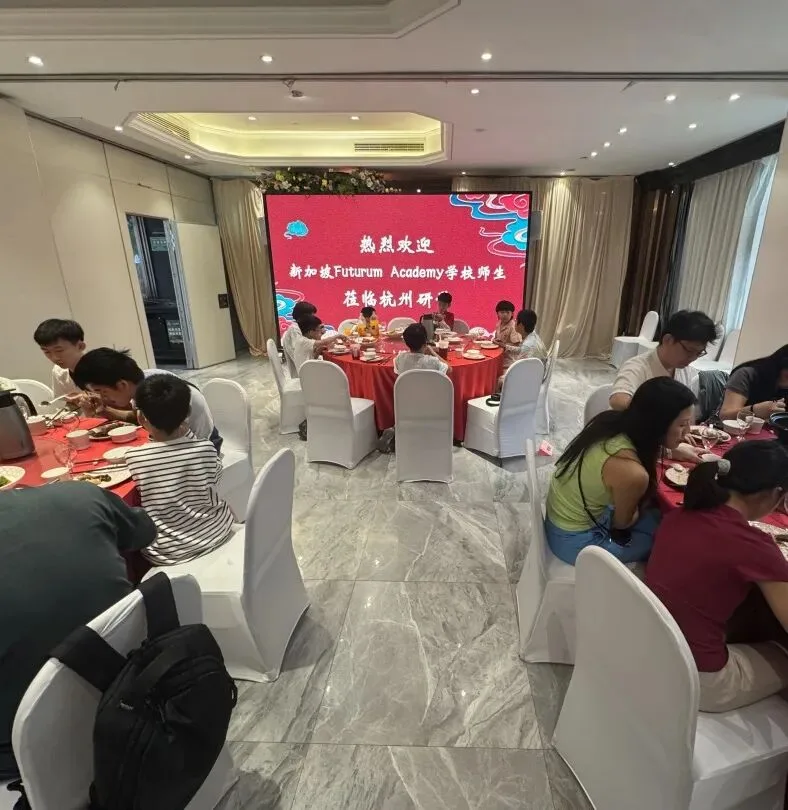 Campers eat at round tables in a banquet room under a screen welcoming Futurum Academy