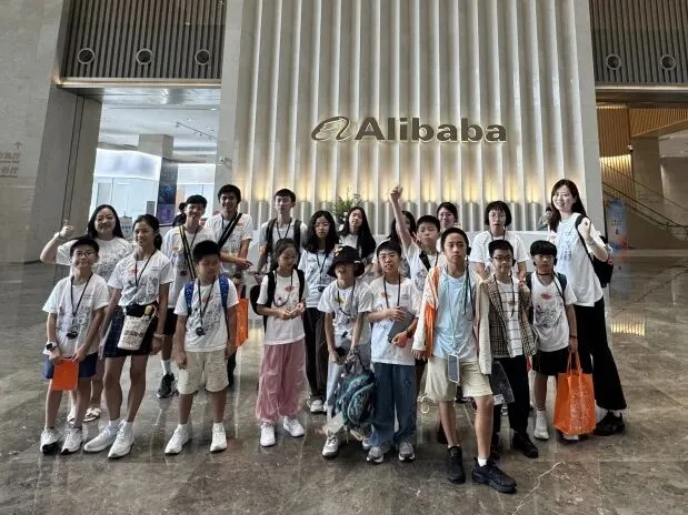 The group poses in the Alibaba headquarters lobby beneath the illuminated Alibaba sign