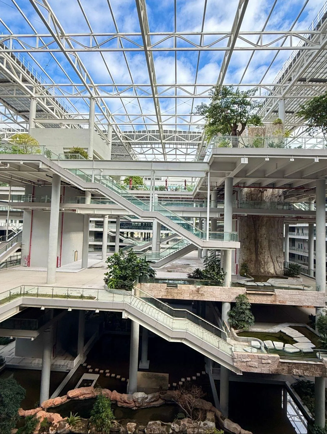 华大园区中庭:玻璃顶棚下层层交错的楼梯、绿植与水景。