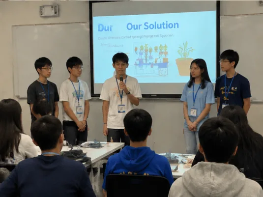 Five students presenting an Our Solution slide illustrating an automatic plant-watering design.