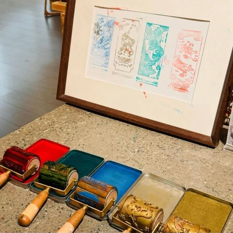 Framed print of four ornamental panels beside inked rollers in red, green, blue and gold trays