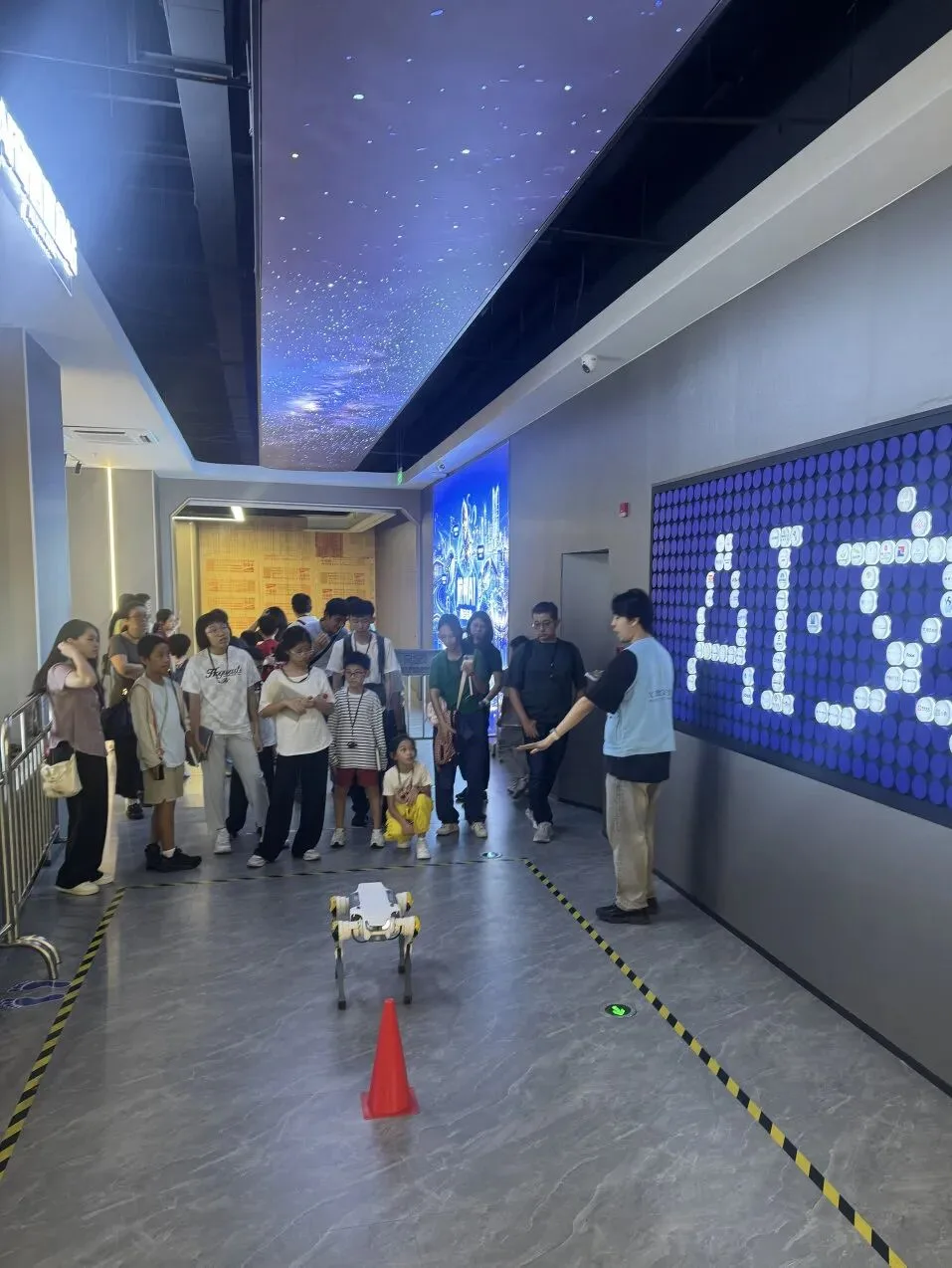 Visitors watch a small quadruped robot cross a corridor beside a blue AI light wall