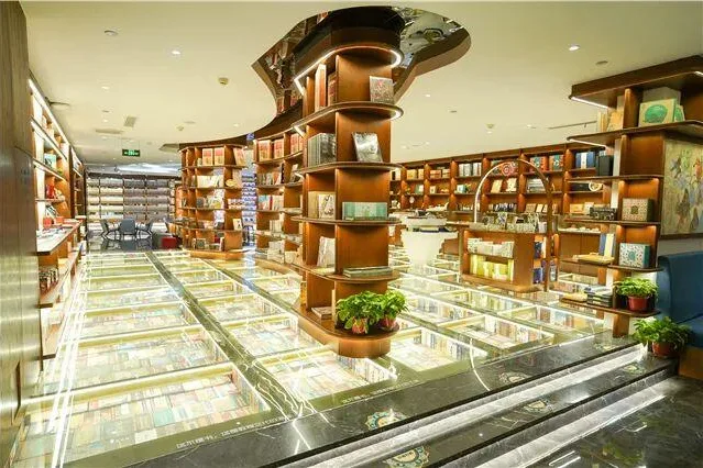 Bookshop hall with a curved tiered display column, glass-floored book vitrines and potted plants