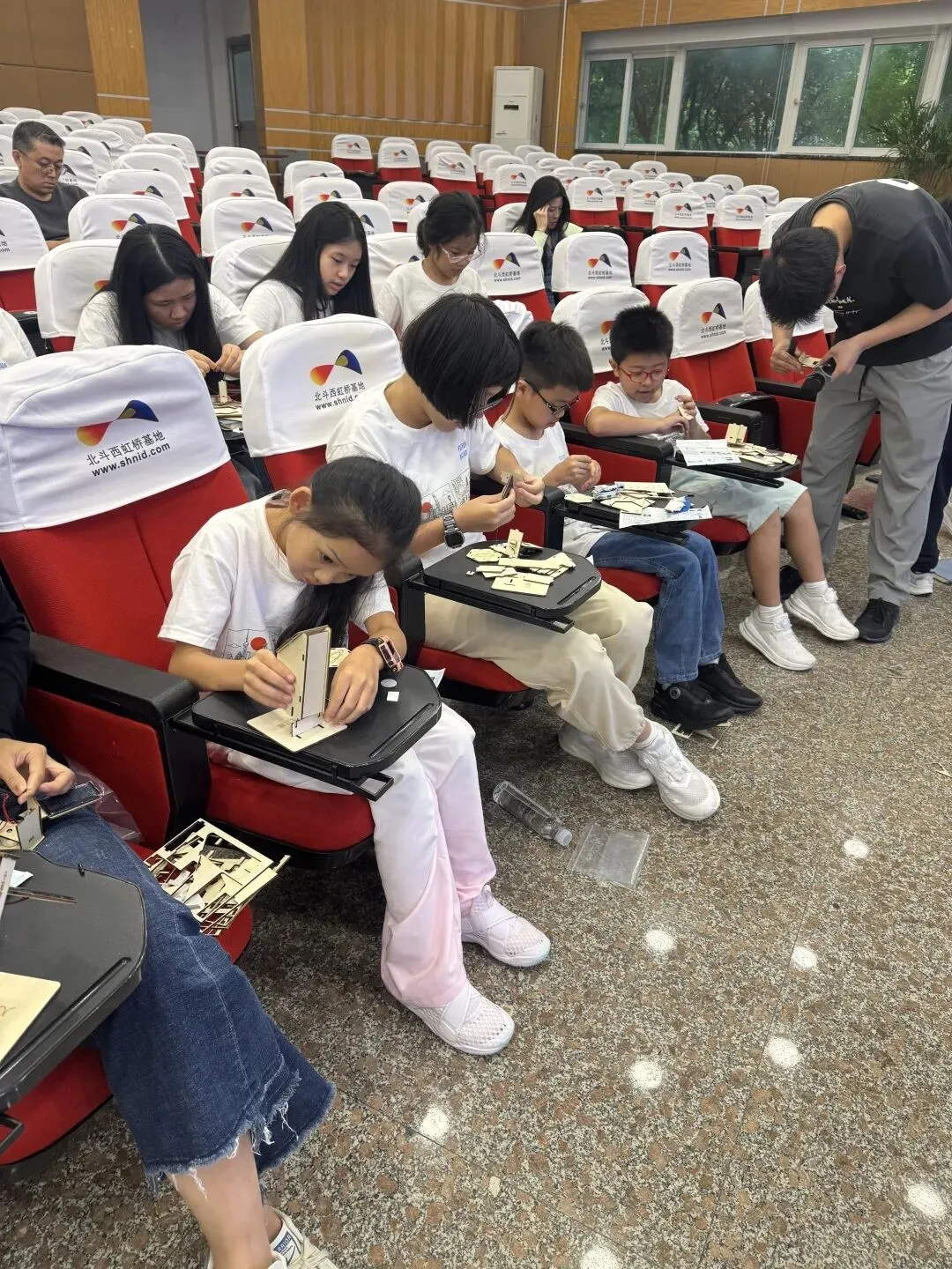 Children assemble wooden satellite kits on the fold-out desks of a lecture theatre