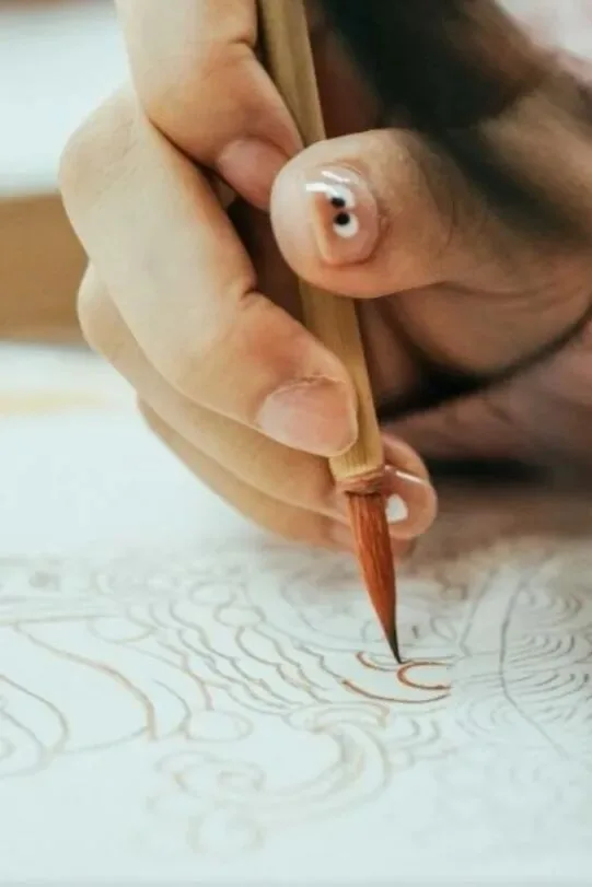 Hand drawing fine outline strokes with a slender brush on a white mural ground