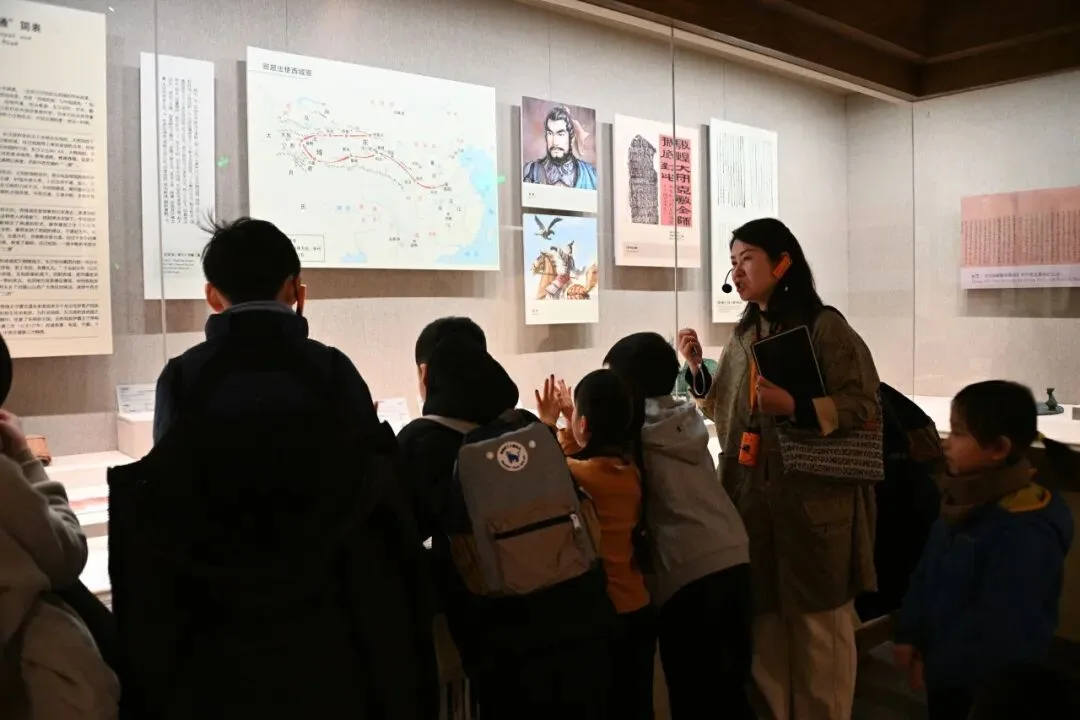 Museum guide at wall panels showing a Silk Road map, an envoy portrait and a camel rider