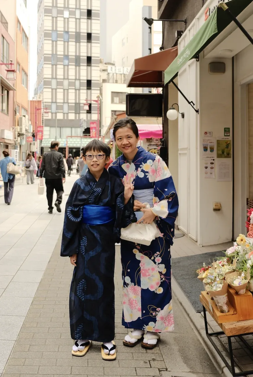 A boy and a woman in indigo yukata on a street beside a flower stall
