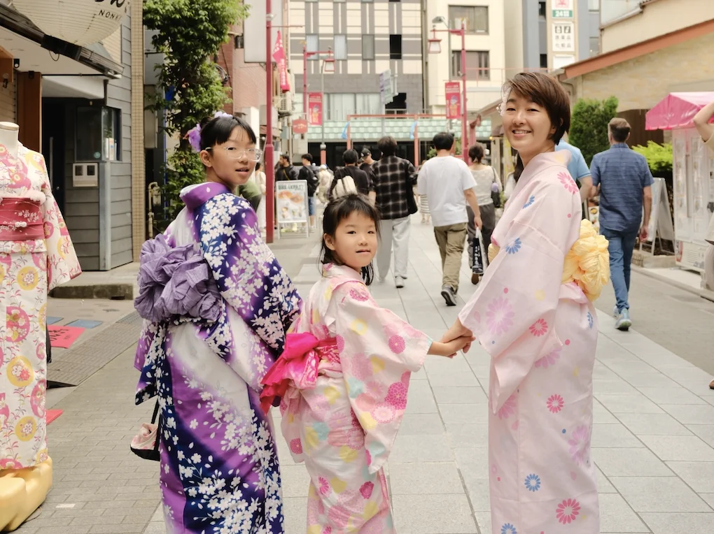 A woman and two girls in yukata glancing back over their shoulders on a busy street