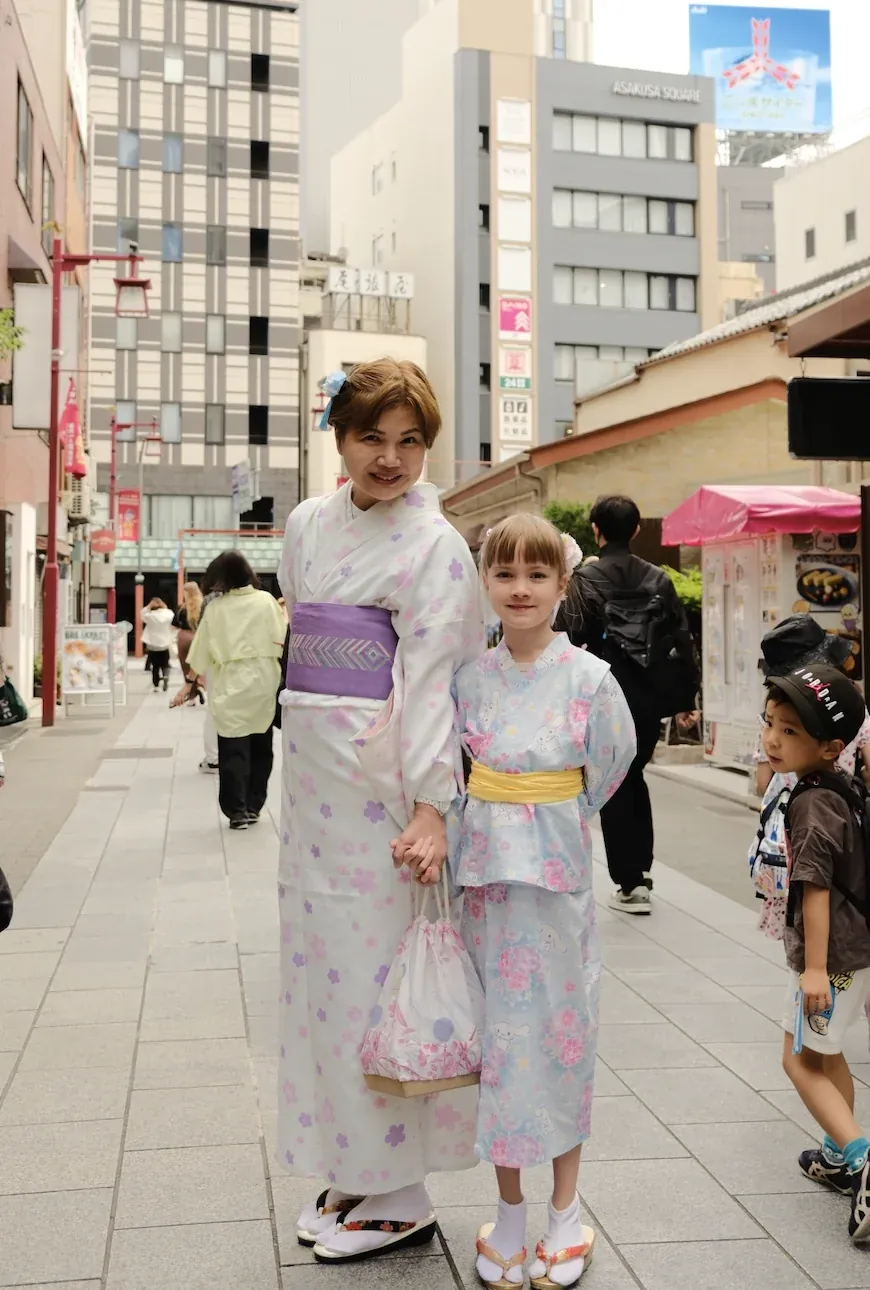 A woman and a girl in pale yukata holding hands on an Asakusa street