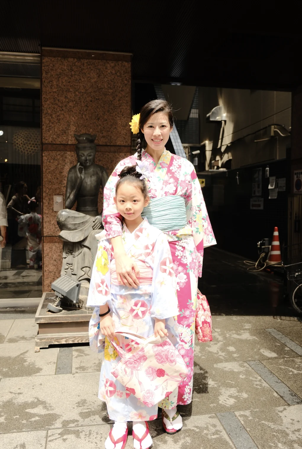 A woman and a girl in matching floral yukata beside a stone statue